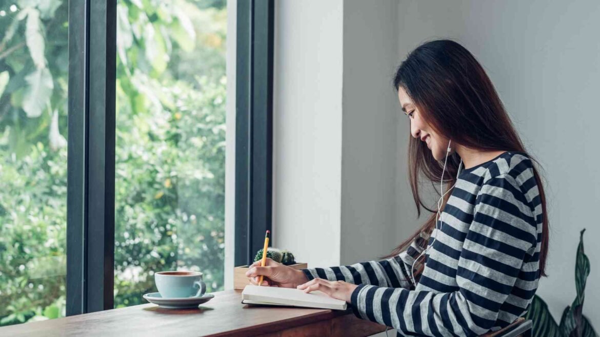 Woman practicing mindful journaling for general health improvement by sunlit window with tea