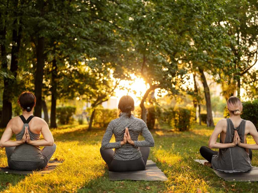 Three women practicing yoga outdoors in a seated pose during sunset, promoting general health and holistic well-being