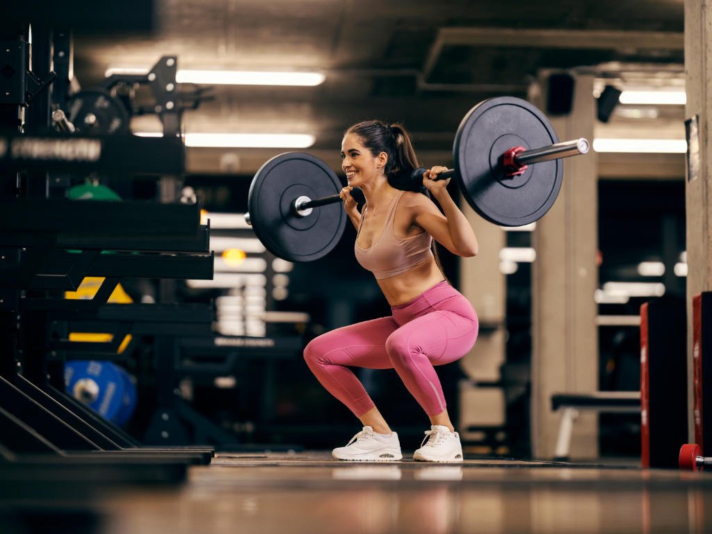 Woman performing barbell squat exercise during strength training session as part of her fitness journey in modern gym