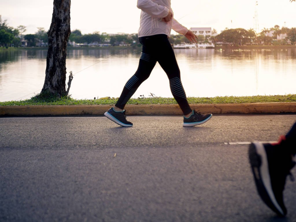 Person doing brisk walking cardio workout along lakeside path at sunset