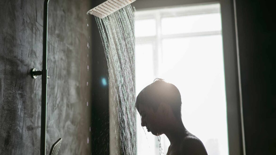 Person experiencing refreshing cold showers with water streaming from modern rainfall showerhead, demonstrating health benefits of cold therapy
