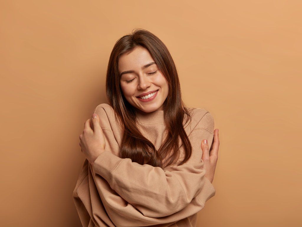 Smiling woman hugging herself, symbolizing self-compassion and emotional wellness