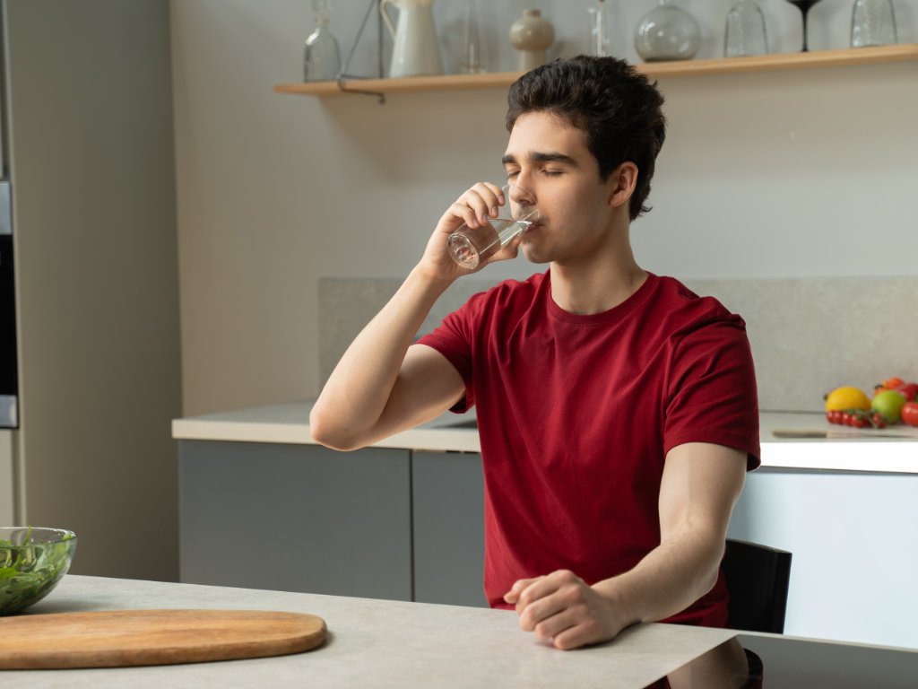 Man practicing habit stacking by drinking water in the kitchen as part of his daily health habits