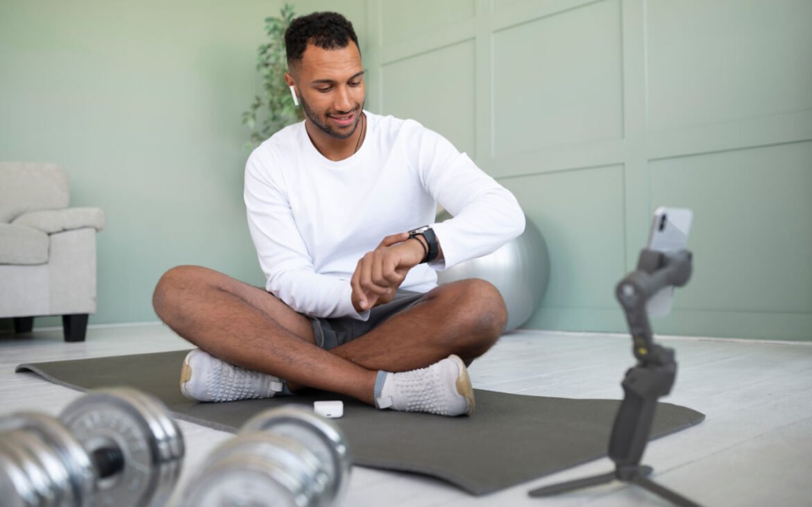 Man in white workout clothes doing home fitness routine for men's health, sitting cross-legged with dumbbells and yoga mat