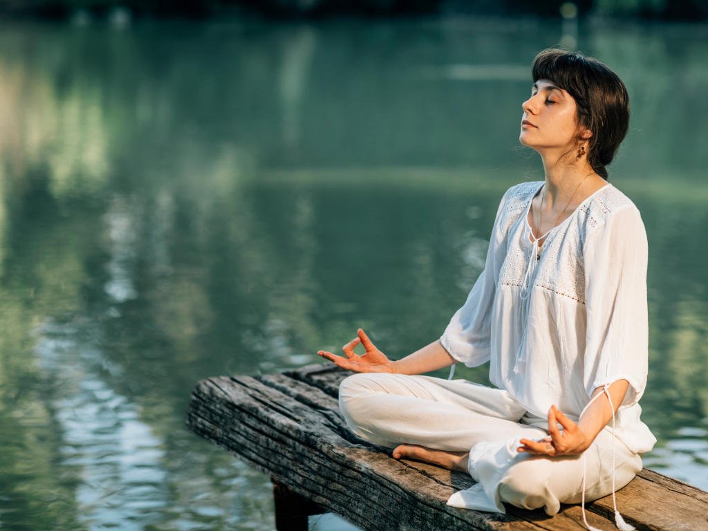 Woman practicing mindfulness meditation by the lake as one of the effective anxiety relief techniques