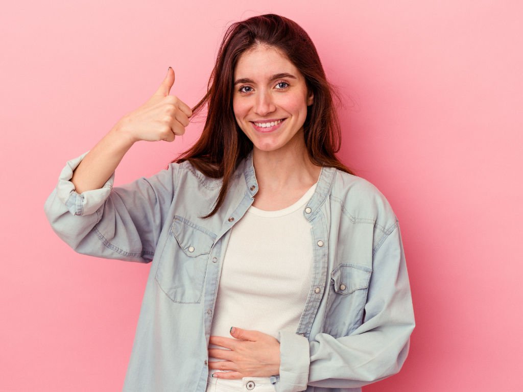 Woman smiling with hand on stomach showing thumbs up for probiotic foods and gut health