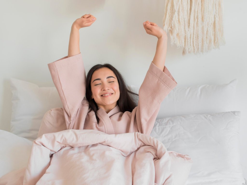 Woman celebrating improved sleep quality with arms raised in bed, showing morning satisfaction and enhanced well-being