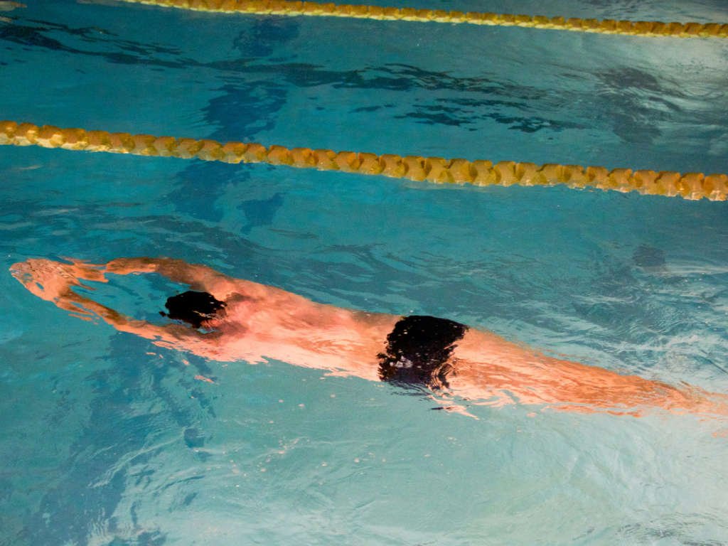 Adult swimmer performing gentle freestyle stroke as part of active post-workout recovery routine in pool