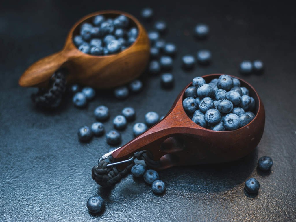 Fresh blueberries in wooden spoons showcasing antioxidant-rich foods with scattered berries on dark surface