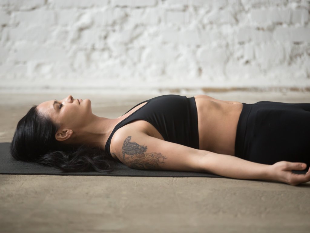 Woman practicing body scan meditation in savasana pose demonstrating mindful meditation benefits for stress relief
