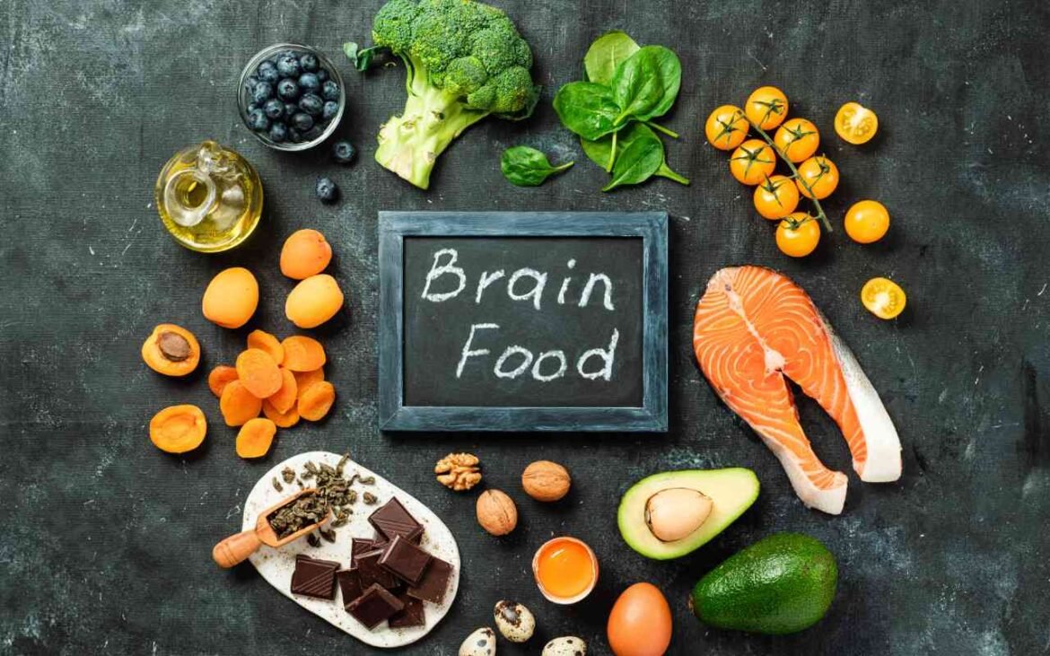 Brain food superfood arrangement with salmon, avocado, broccoli, berries, nuts and dark chocolate around chalkboard sign for enhanced mental focus