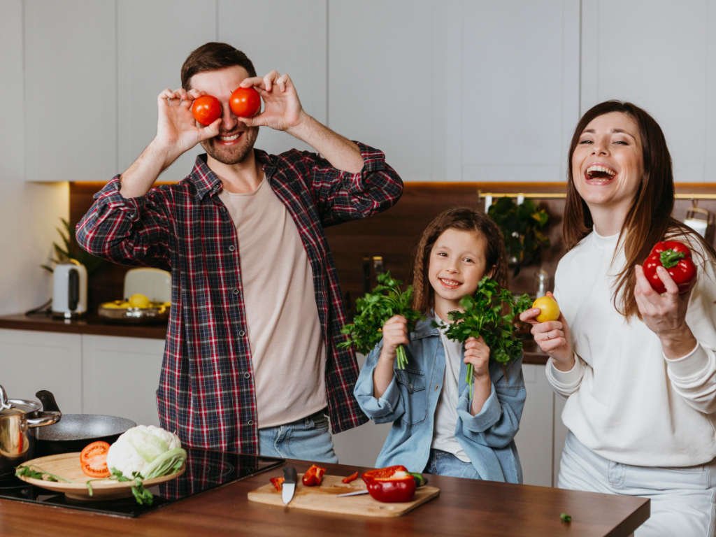 Happy family playing with fresh vegetables while cooking together, building lifetime health habits through positive family dynamics
