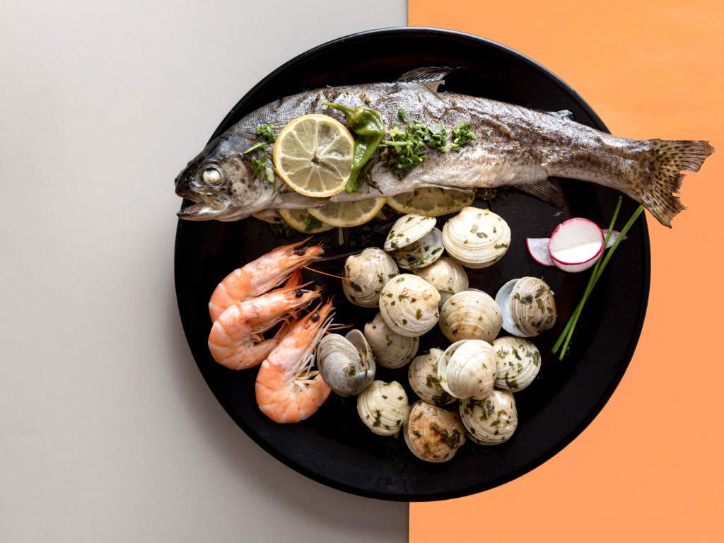 Fresh fish and shellfish metabolism boosting foods including whole fish, shrimp and clams on black plate for rapid weight loss