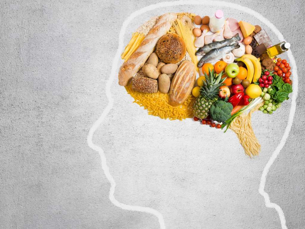 Foods for mental clarity arranged in brain shape including fish, fruits, vegetables, nuts, and whole grains on white background