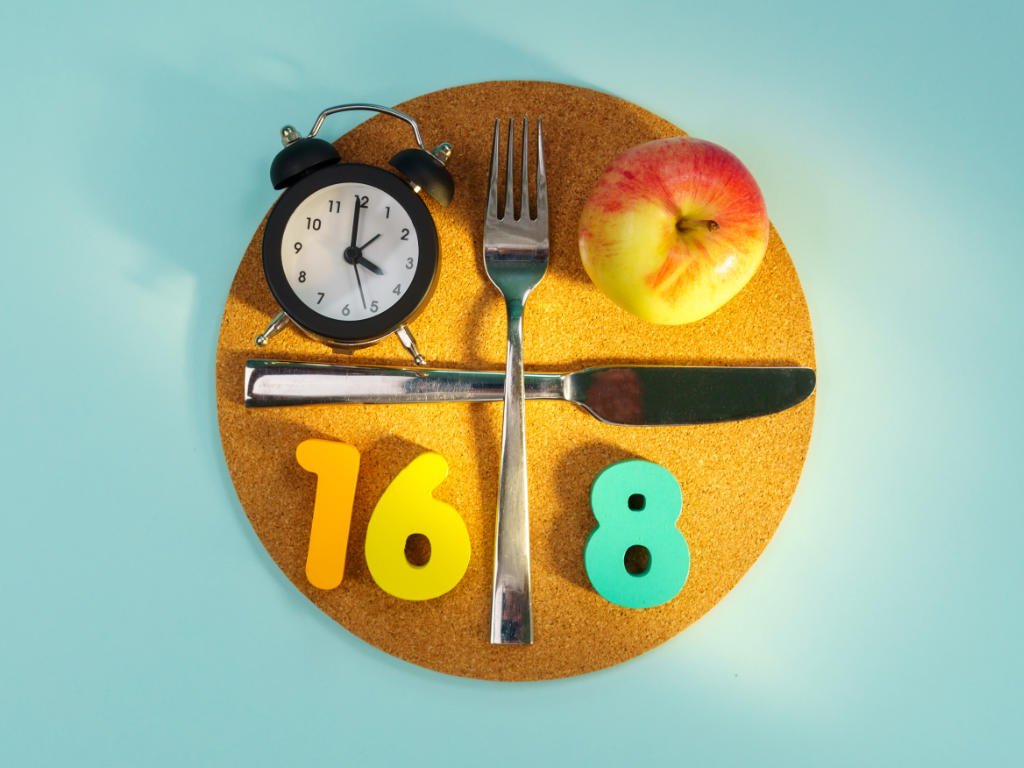 Intermittent fasting concept showing 16:8 meal timing with healthy foods that boost weight loss including fresh apple and eating utensils arranged on clock face