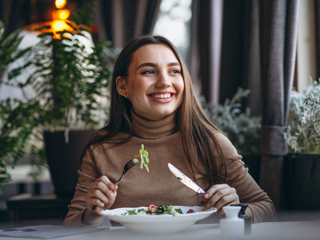 Woman practicing mindfulness techniques while eating healthy salad in cozy restaurant setting