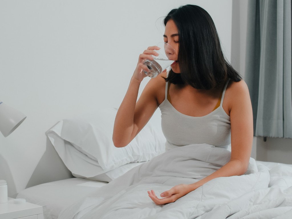 Woman drinking fresh water in bed as essential morning lifetime health habit