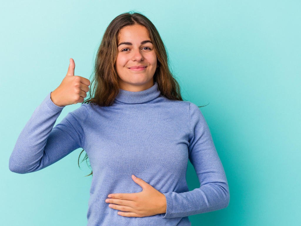 Young woman smiling with hand on stomach and thumbs up, symbolizing improved digestive health from probiotics for women