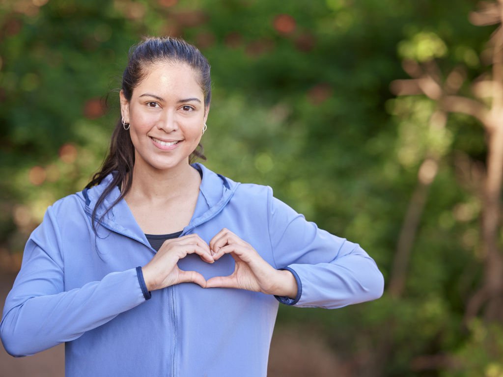 Healthy woman showing heart sign outdoors, symbolizing internal wellness and balanced microbiome – Probiotics for Women