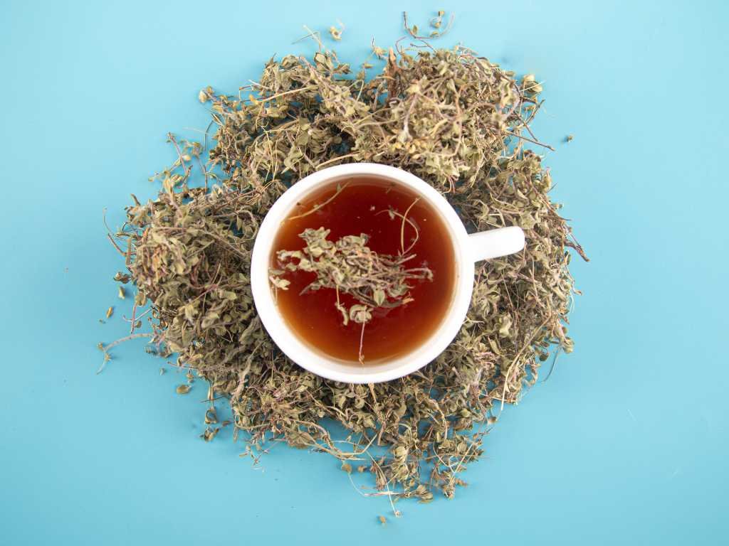 Valerian root teas for anxiety relief with dried herbal ingredients surrounding white teacup on blue background