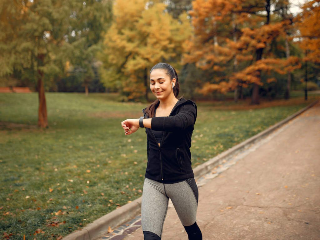 Woman checking fitness tracker in park while building sustainable exercise routine for effective weight loss in your 40s