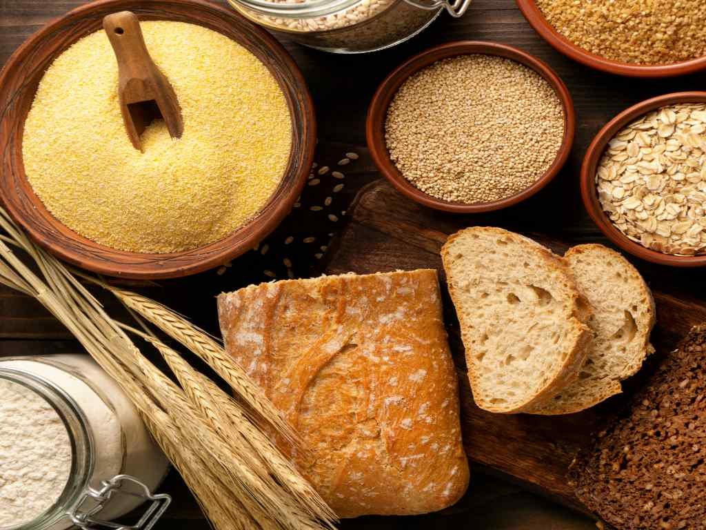 Assortment of metabolism boosting foods including whole grain bread, oats, quinoa, and various unprocessed grains compared to refined flour in glass jars