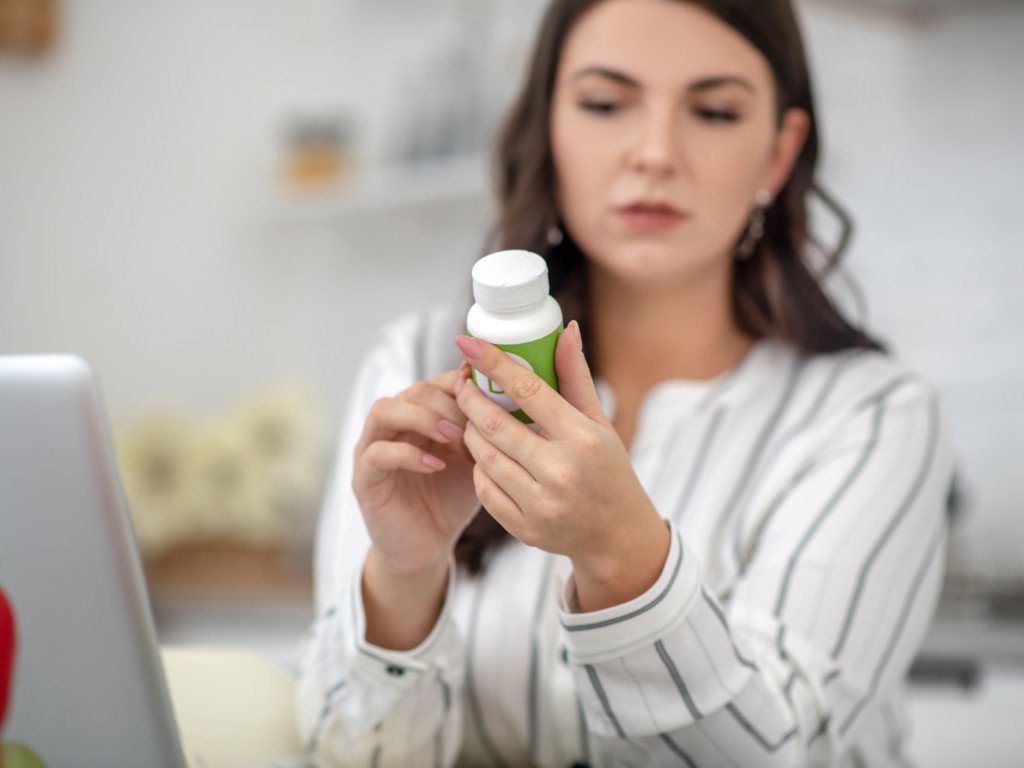 Woman carefully reading Omega-3 supplement label to check quality and benefits information