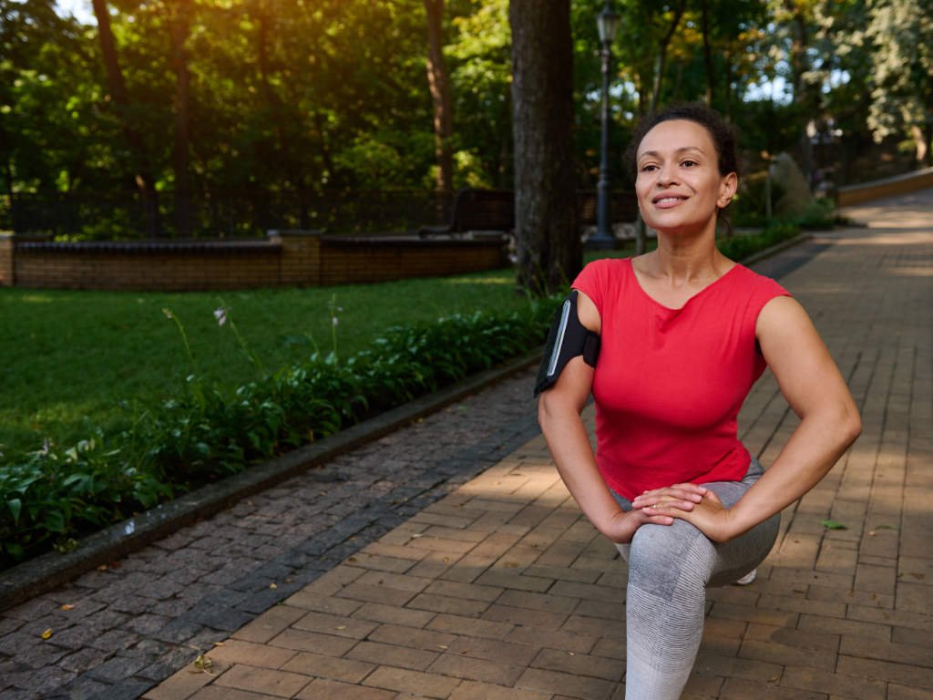 Active woman in her twenties performing exercises for women's fitness outdoors in park setting demonstrating age-appropriate workout routines