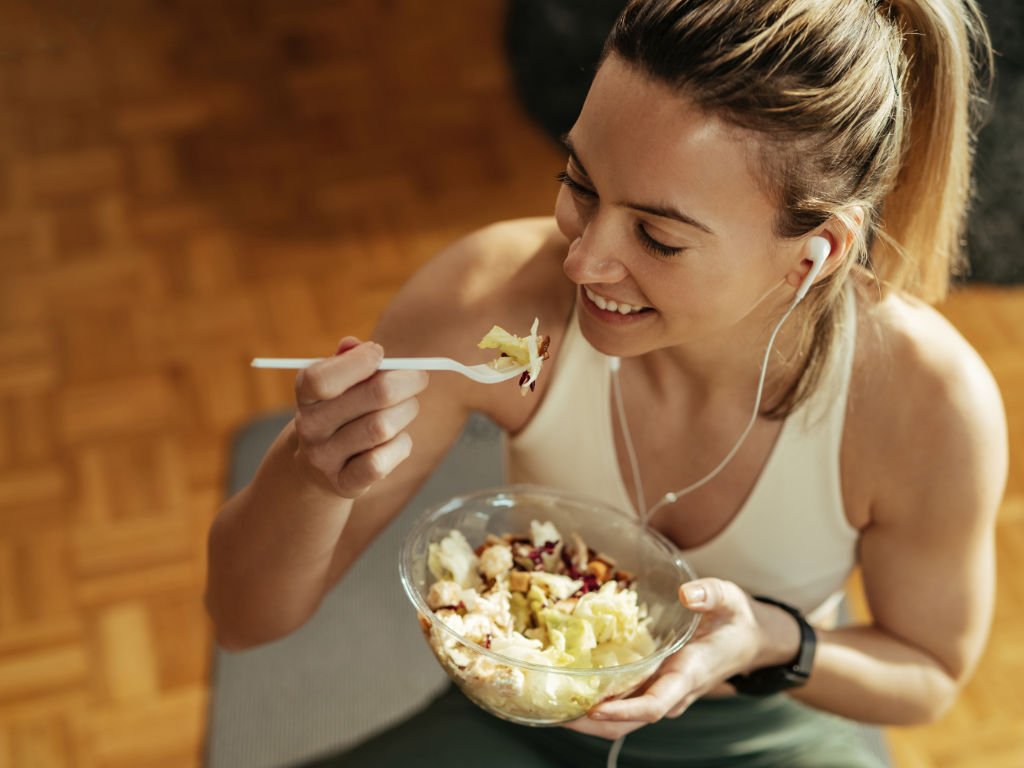 Smiling woman in athletic wear enjoying nutritious bowl meal to support exercises for women's fitness goals and recovery