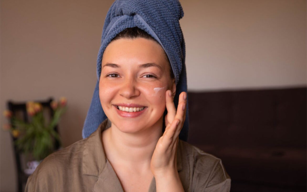 Woman applying anti-aging skincare cream with towel wrap showing radiant glowing skin