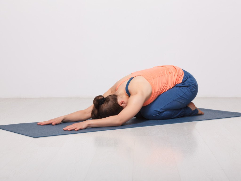 Woman demonstrating Child's Pose yoga for mental clarity and stress relief on blue yoga mat