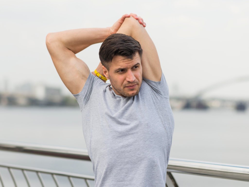 Man performing dynamic stretching exercises for shoulders and triceps during outdoor warm-up routine