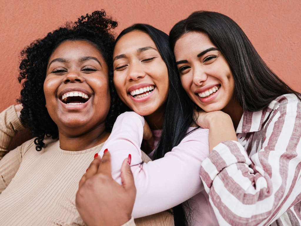 Three diverse women laughing together demonstrating how social connections help combat stress and promote mental wellness