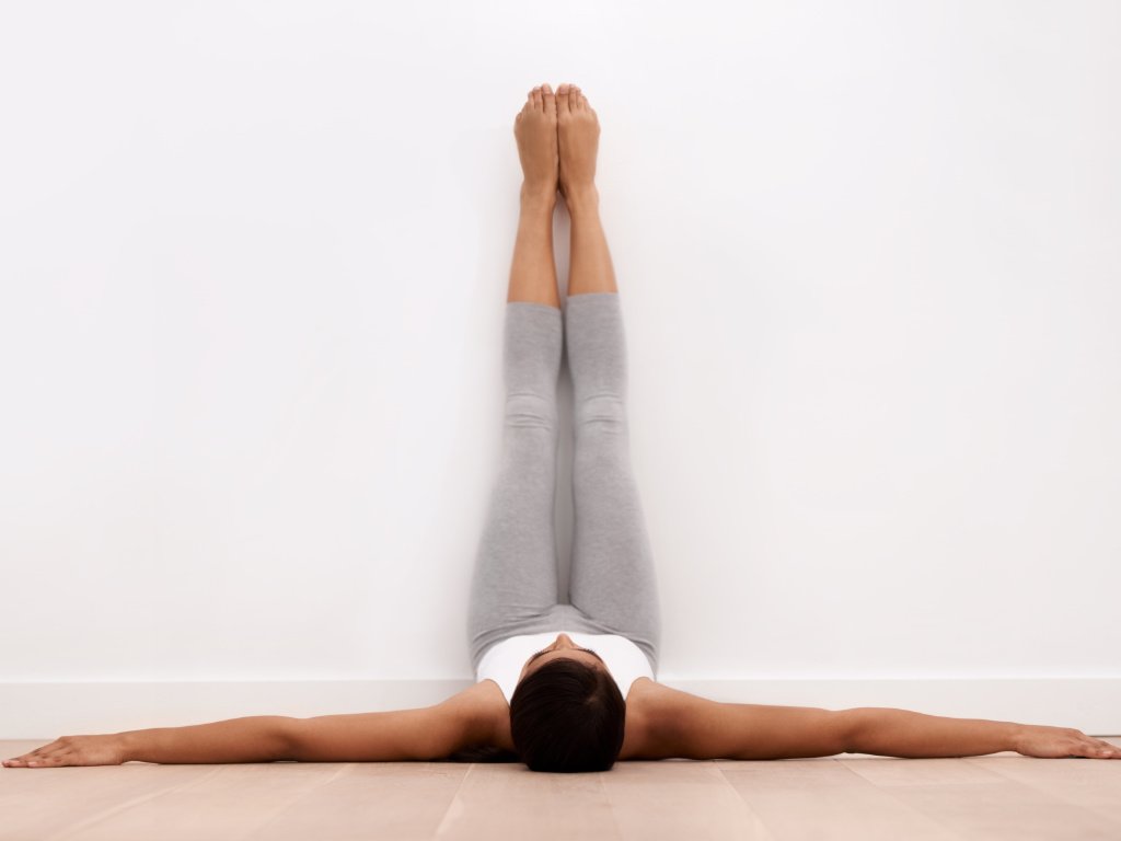 Woman practicing Legs-Up-The-Wall yoga pose for mental clarity and stress relief in peaceful white studio