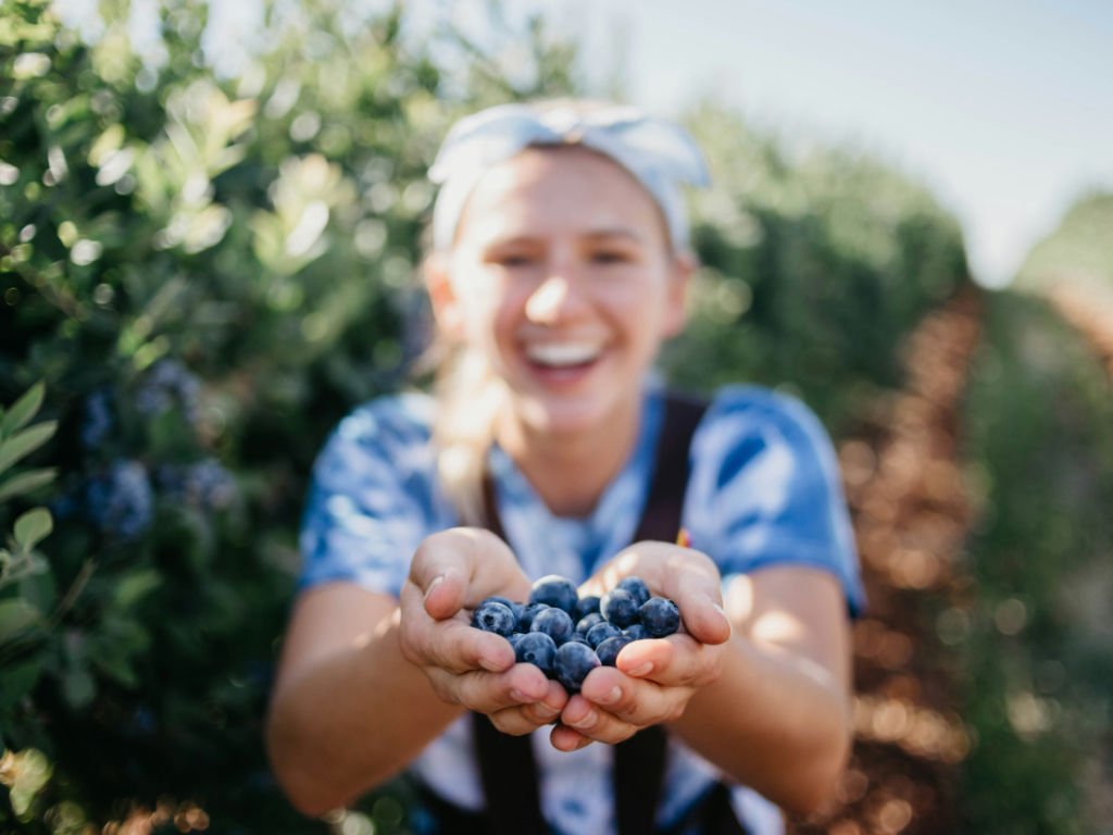 Young woman holding fresh blueberry superfoods ideal for women in their reproductive years (20s-40s) for optimal health