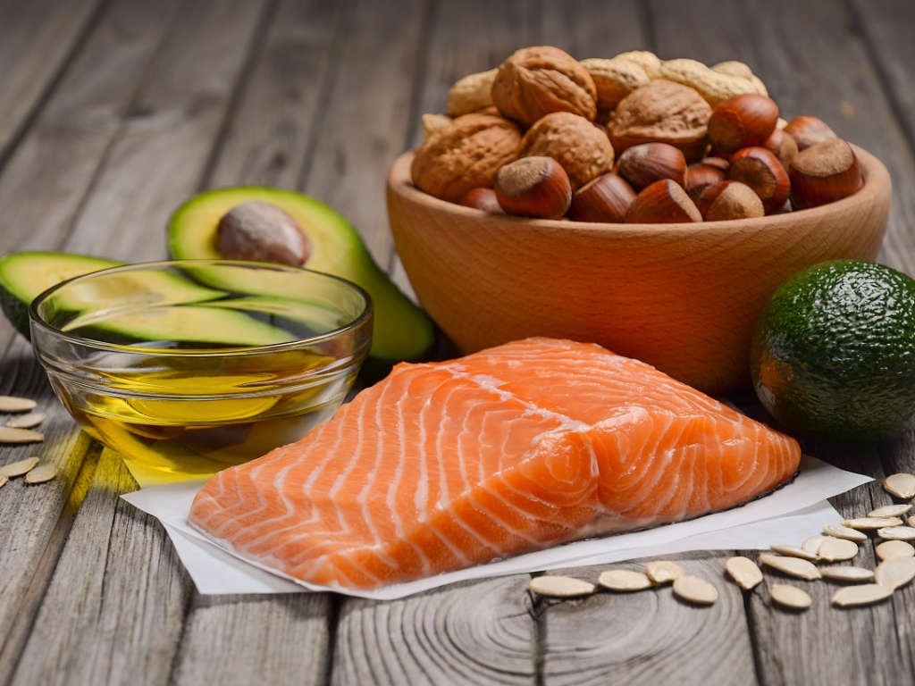 Superfoods for women including fresh salmon, avocado, mixed nuts and olive oil arranged on wooden surface for natural skin glow