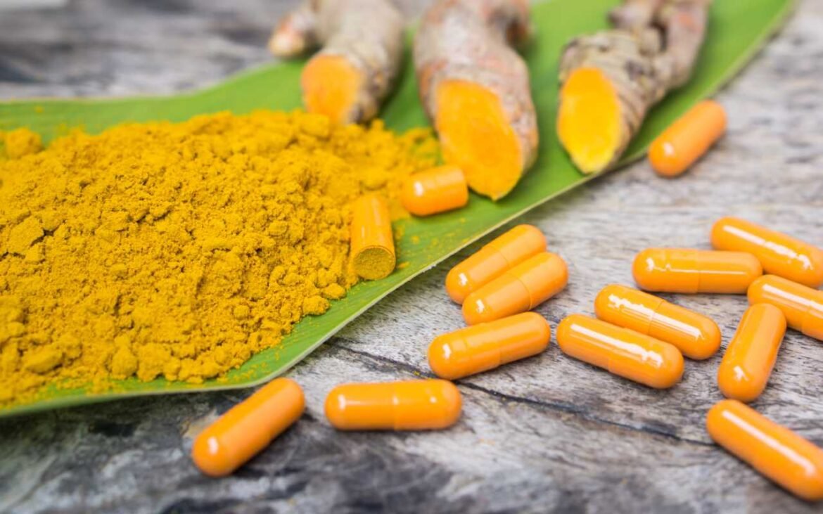 Turmeric supplements in capsule form with turmeric powder and fresh roots on a leaf – a natural health remedy