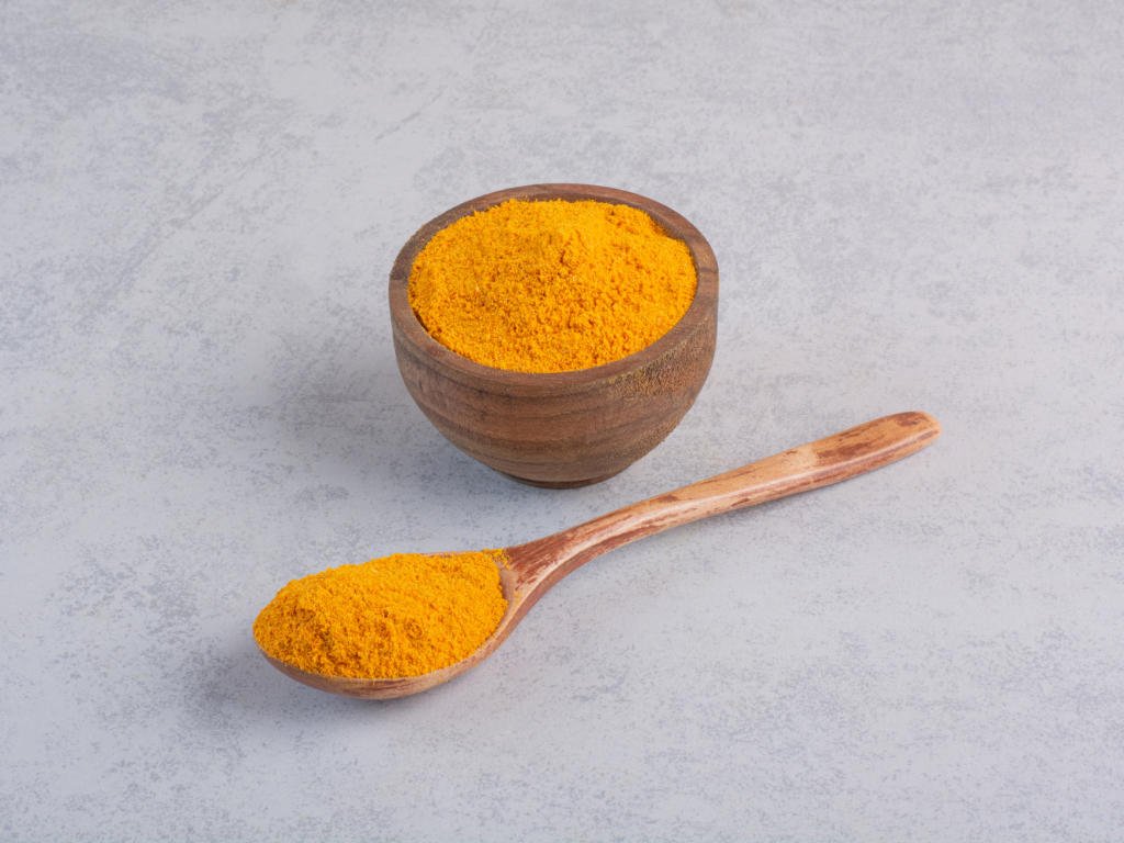 Golden turmeric powder in wooden bowl and spoon showcasing the curcumin compound used in turmeric supplements for health benefits