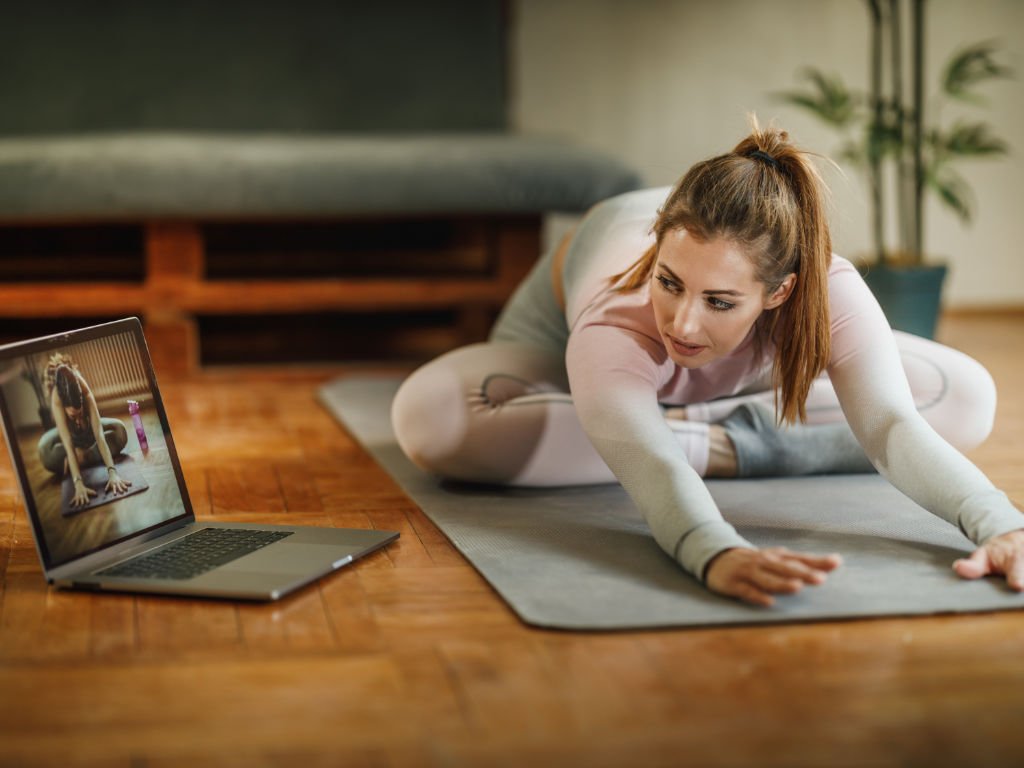 Professional woman following ultimate fitness virtual personal training session with online instructor via laptop