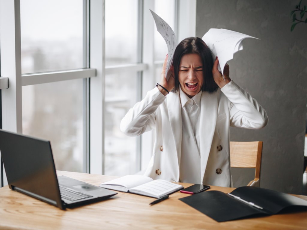 Overwhelmed professional woman with papers flying demonstrating why we need to combat stress more than ever in modern workplace