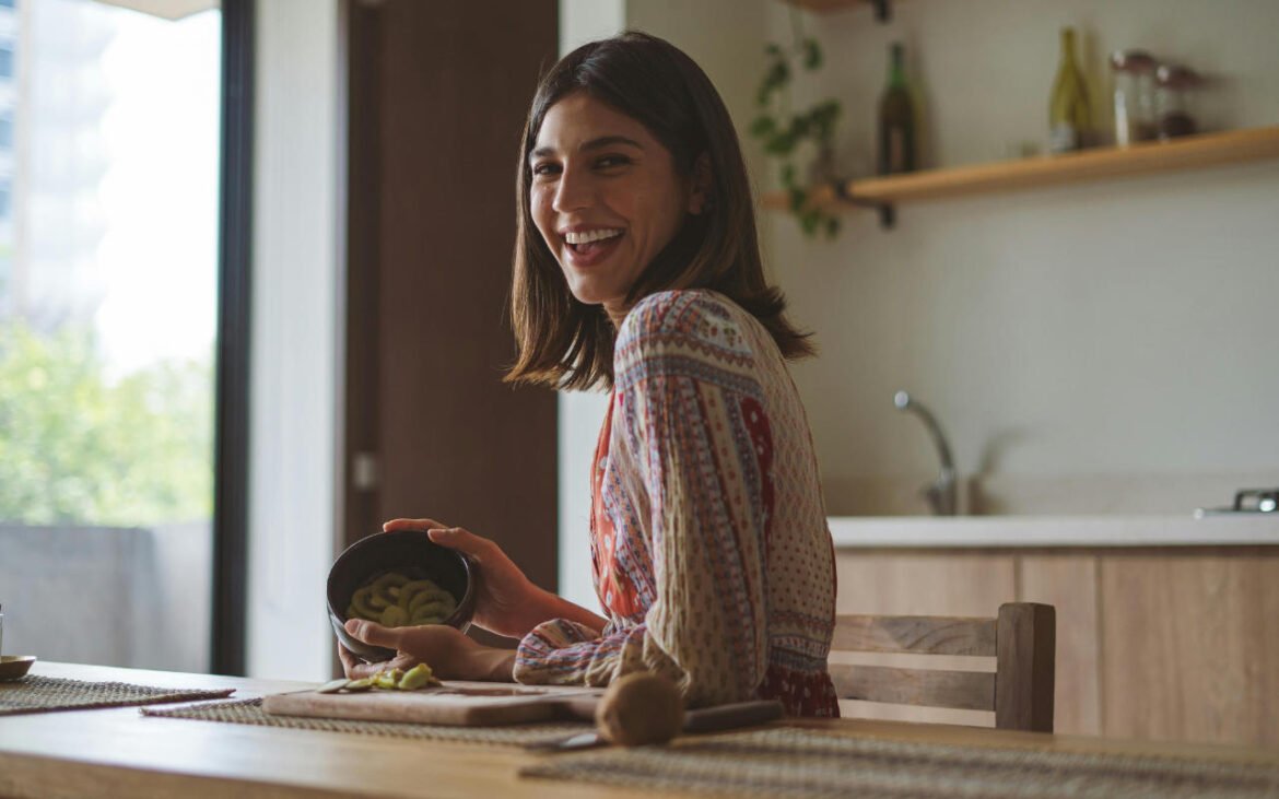 Happy woman holding bowl of superfoods in modern kitchen - healthy eating for woman wellness