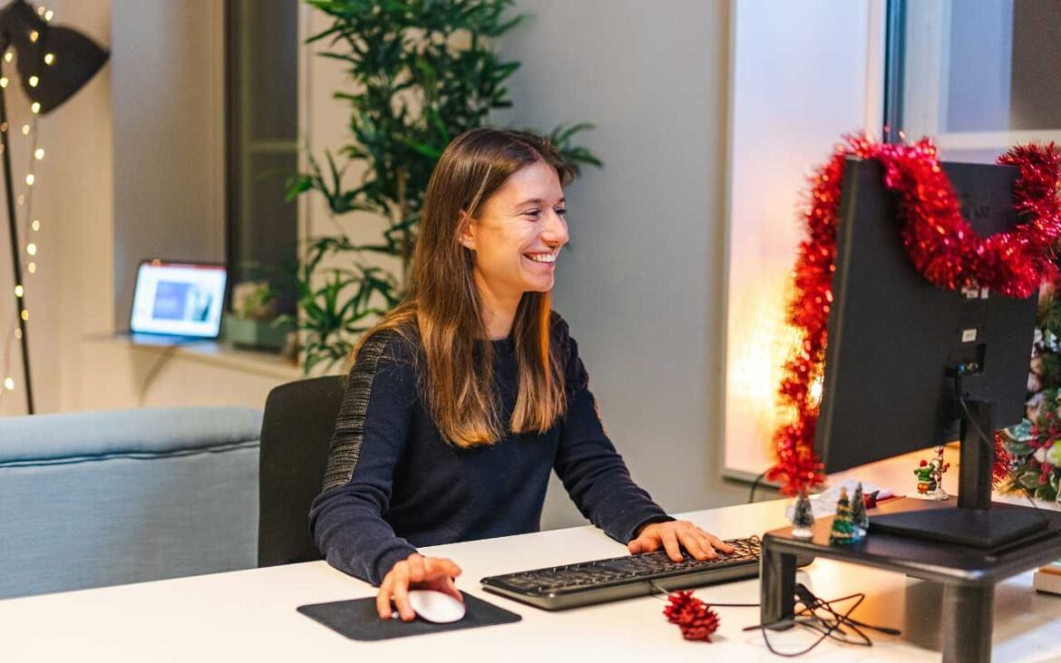 Smiling woman working at her desk demonstrating emotional wellness at work in a comfortable office environment with festive decorations