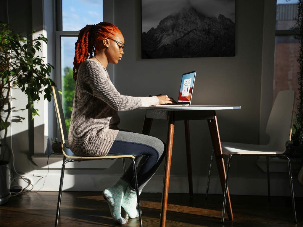 Professional woman working peacefully at laptop in bright office space with plants, demonstrating emotional wellness at work through calm and focused environment