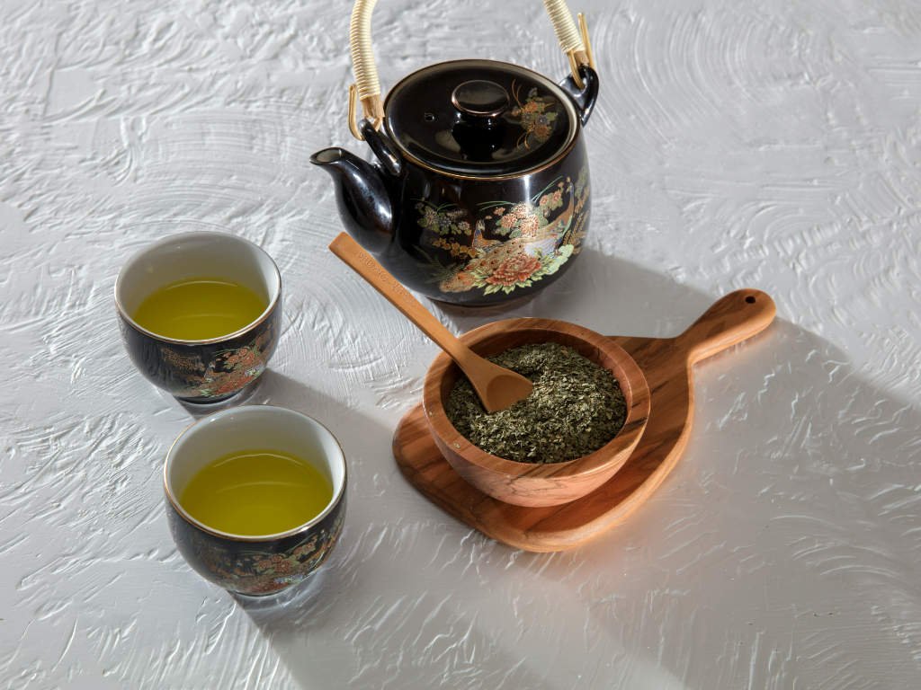 Traditional green tea ceremony setup showing herbal teas for focus with loose tea leaves and brewing essentials on white textured surface