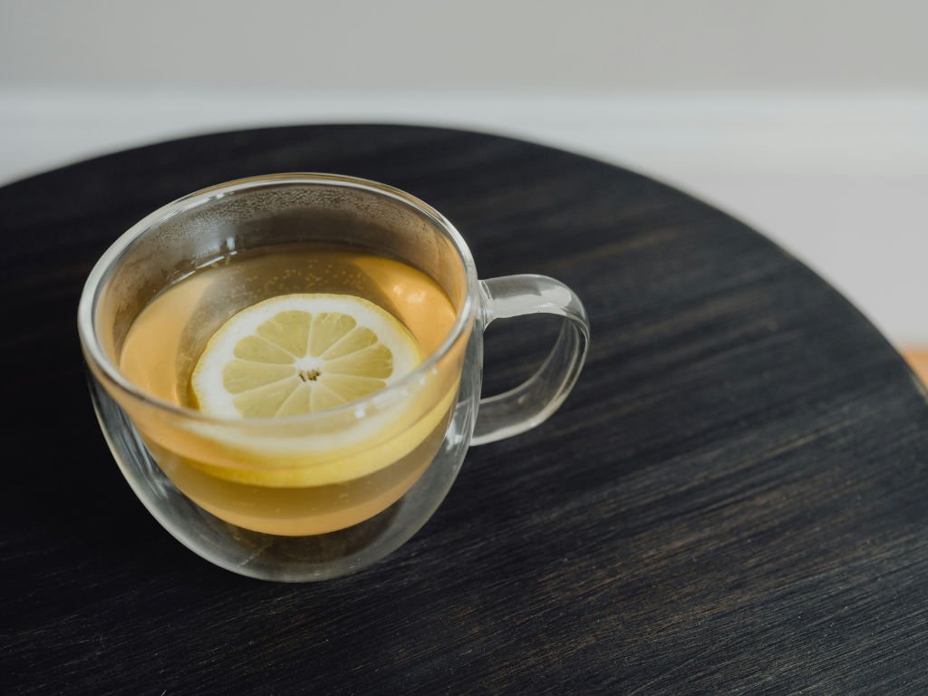 Clear glass mug of golden lemon balm tea with fresh lemon slice, one of the top herbal teas for focus and mental clarity