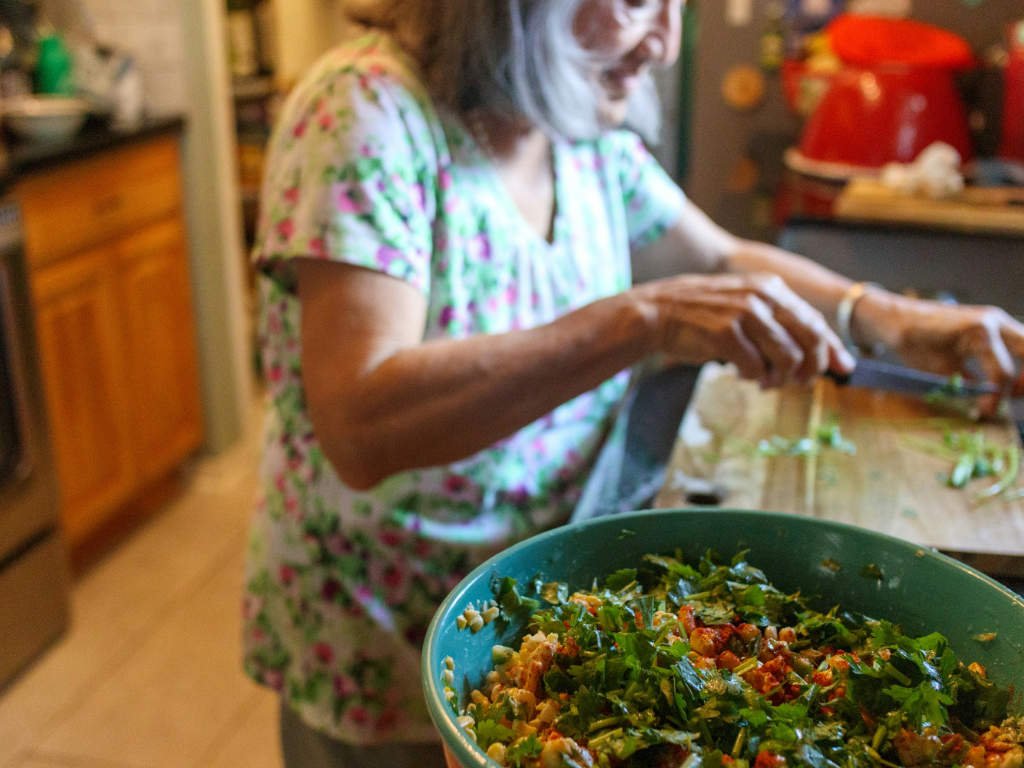 Older adult preparing fresh vegetable salad as part of long-term health strategies for age-specific nutritional needs