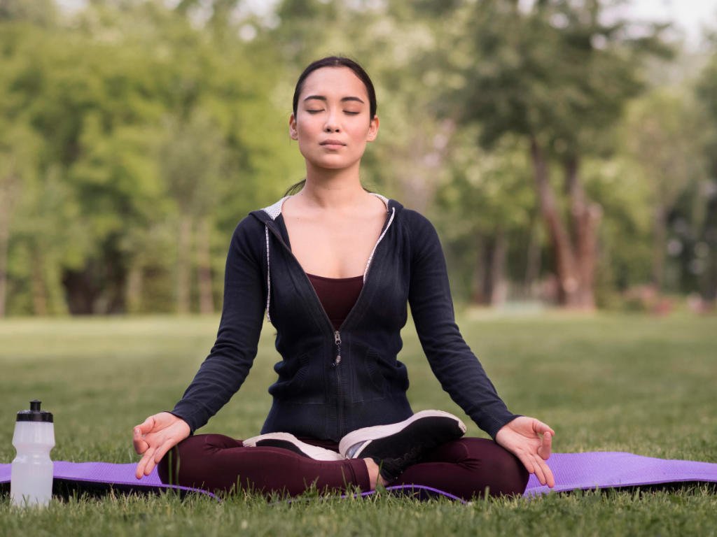 Woman demonstrating proper meditation techniques in peaceful outdoor park setting showcasing mental health benefits endorsed by medical professionals