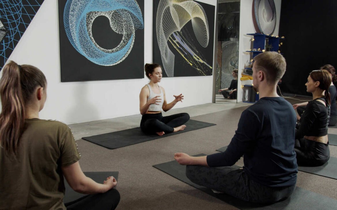Professional instructor teaching powerful meditation techniques to group of students sitting cross-legged on yoga mats in modern wellness studio