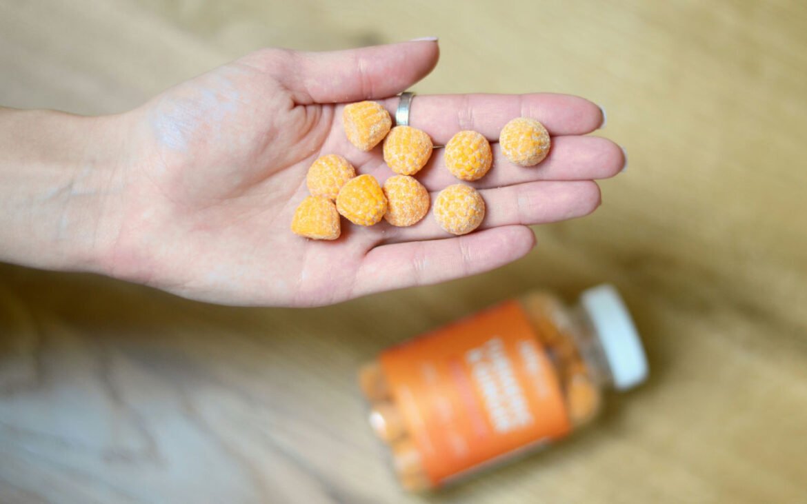 Hand holding yellow probiotic supplements capsules with supplement bottle in background for optimal gut health