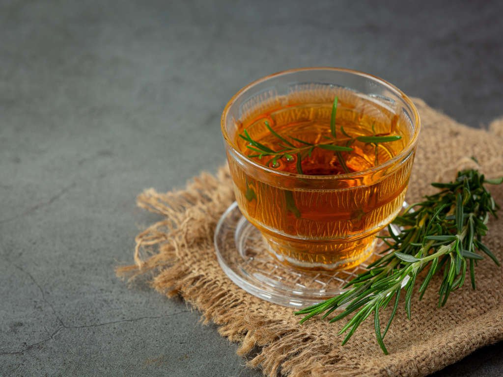 Glass cup of golden rosemary herbal teas for focus with fresh rosemary sprigs showing aromatic focus-boosting properties